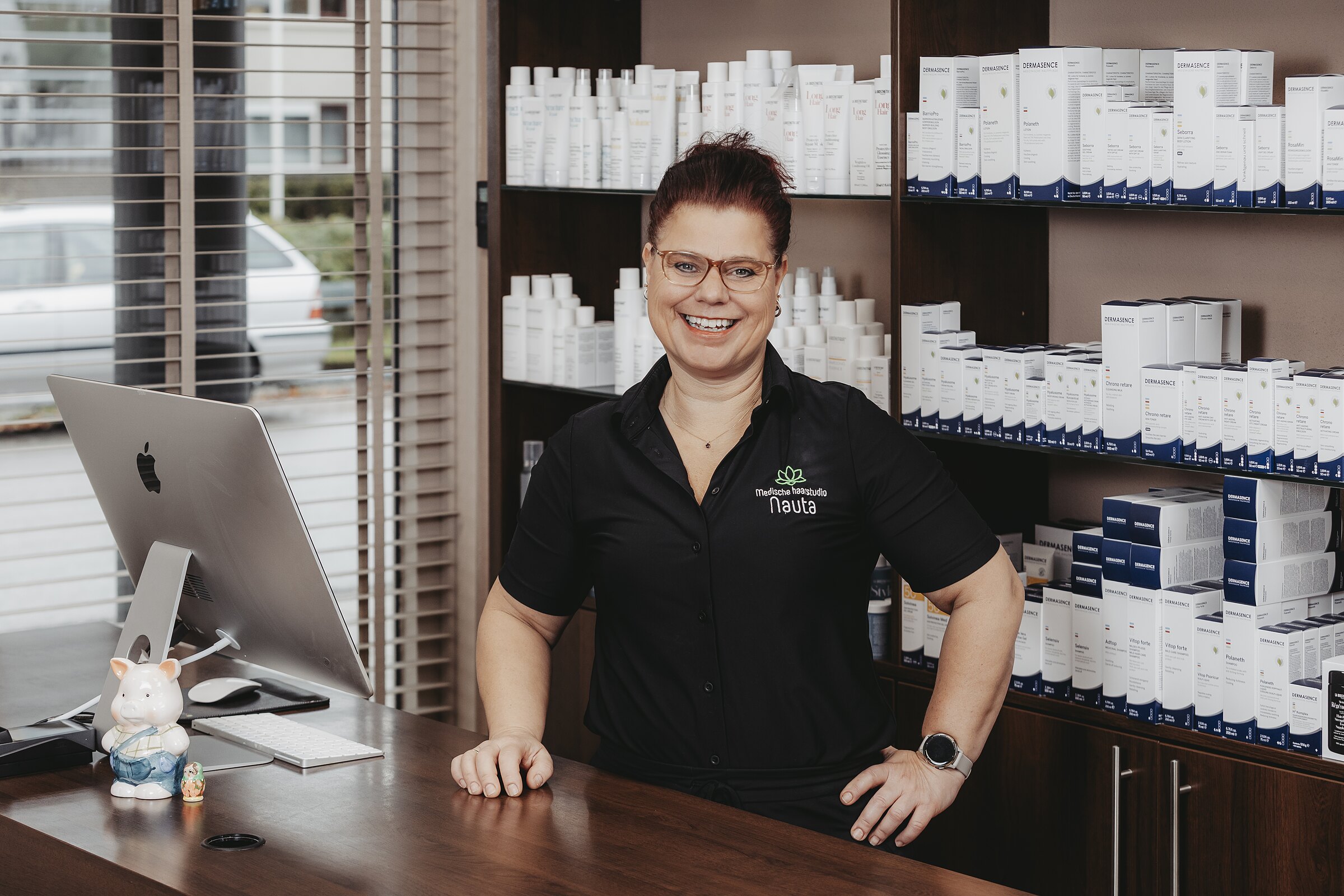 Ellen achter de balie van Medische Haarstudio Nauta, met de productenwand van La Biosthetique